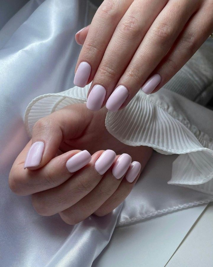 Manos con uñas pintadas de color rosa pálido sosteniendo una flor blanca sobre tela de satén.