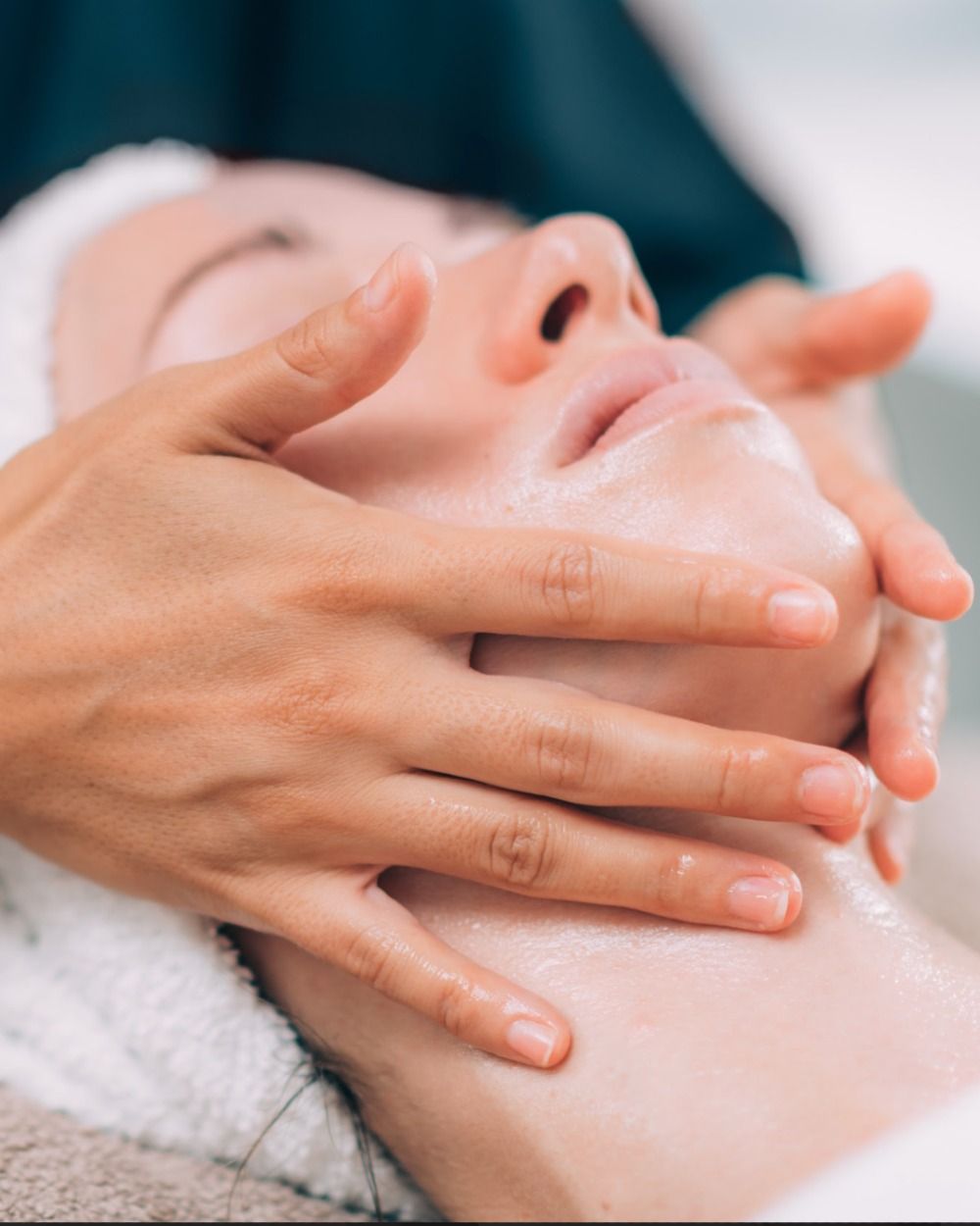Manos masajeando el rostro cubierto de espuma durante un tratamiento facial en un spa.