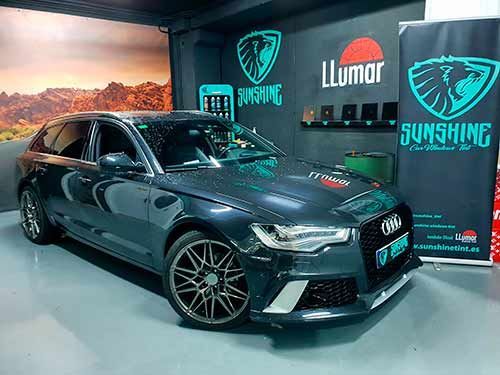 Un Audi A6 negro está aparcado en un garaje junto a un cartel que dice