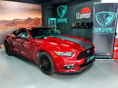 Un mustang rojo está estacionado en un garaje al lado de un cartel que dice