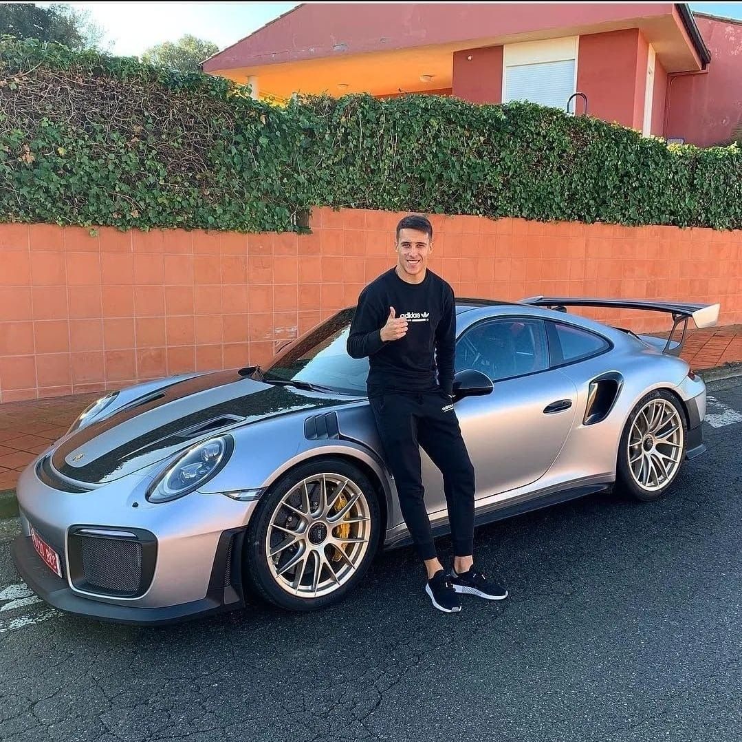 Un hombre está parado frente a un coche deportivo plateado.