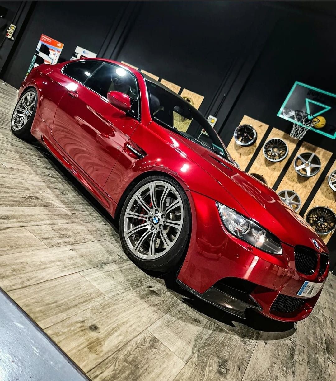 Un BMW M3 rojo está estacionado sobre un piso de madera en un garaje.