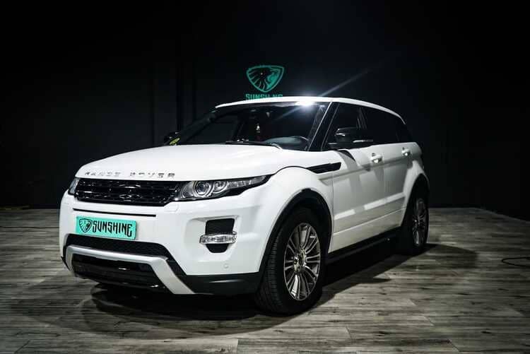 Un Range Rover Evoque blanco está estacionado sobre un piso de madera en una habitación oscura.