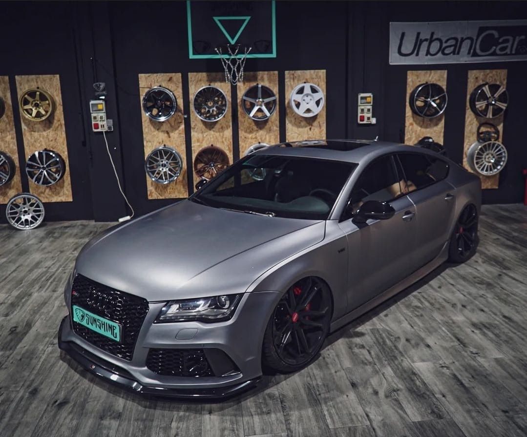 Un coche gris está aparcado delante de un aro de baloncesto.