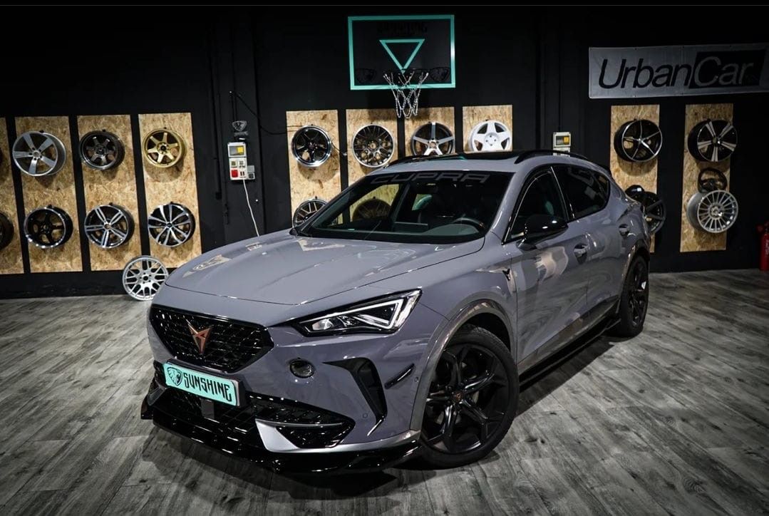 Un coche gris está aparcado en un garaje al lado de una pared de ruedas.