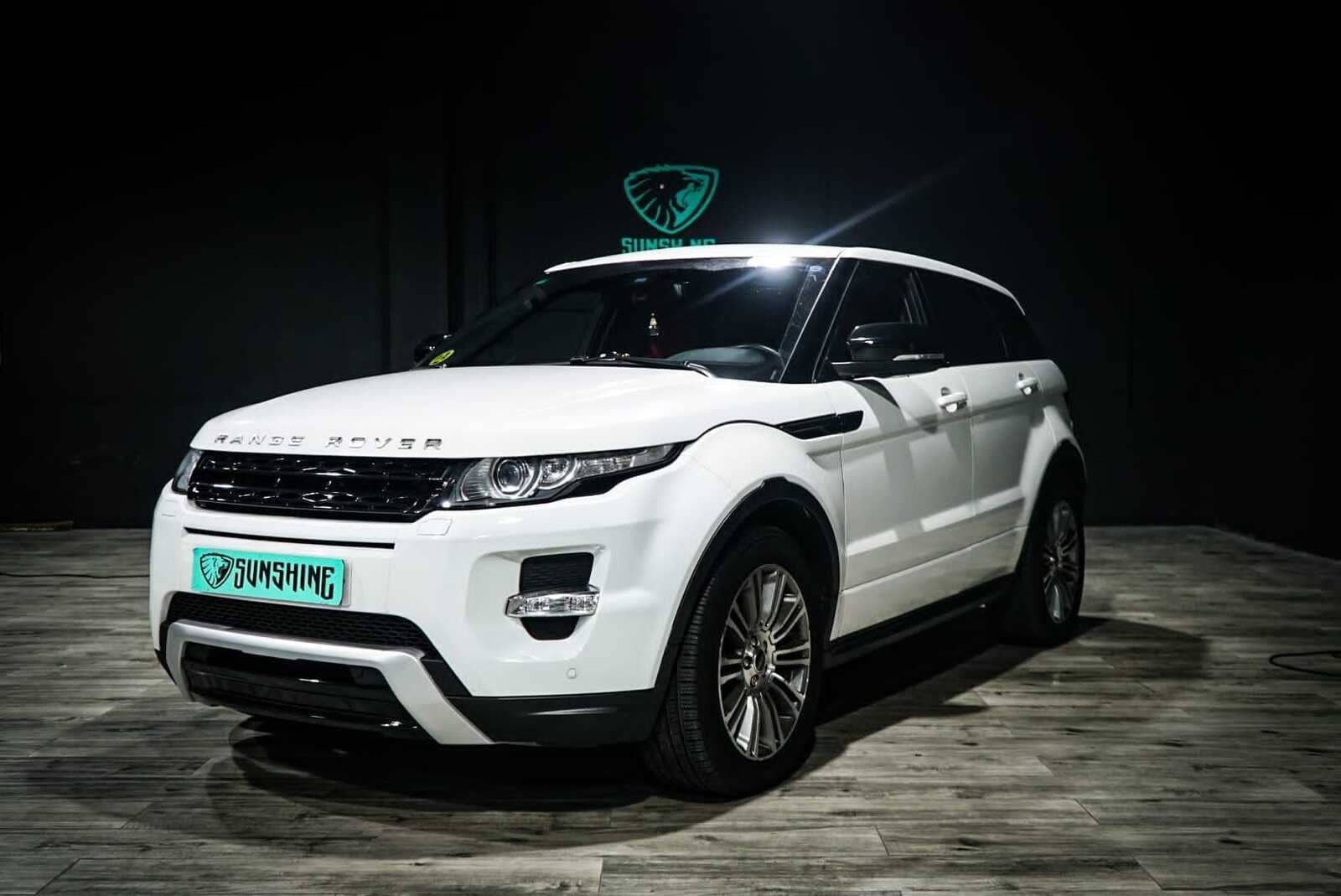 Un Range Rover Evoque blanco está estacionado sobre un piso de madera en una habitación oscura.