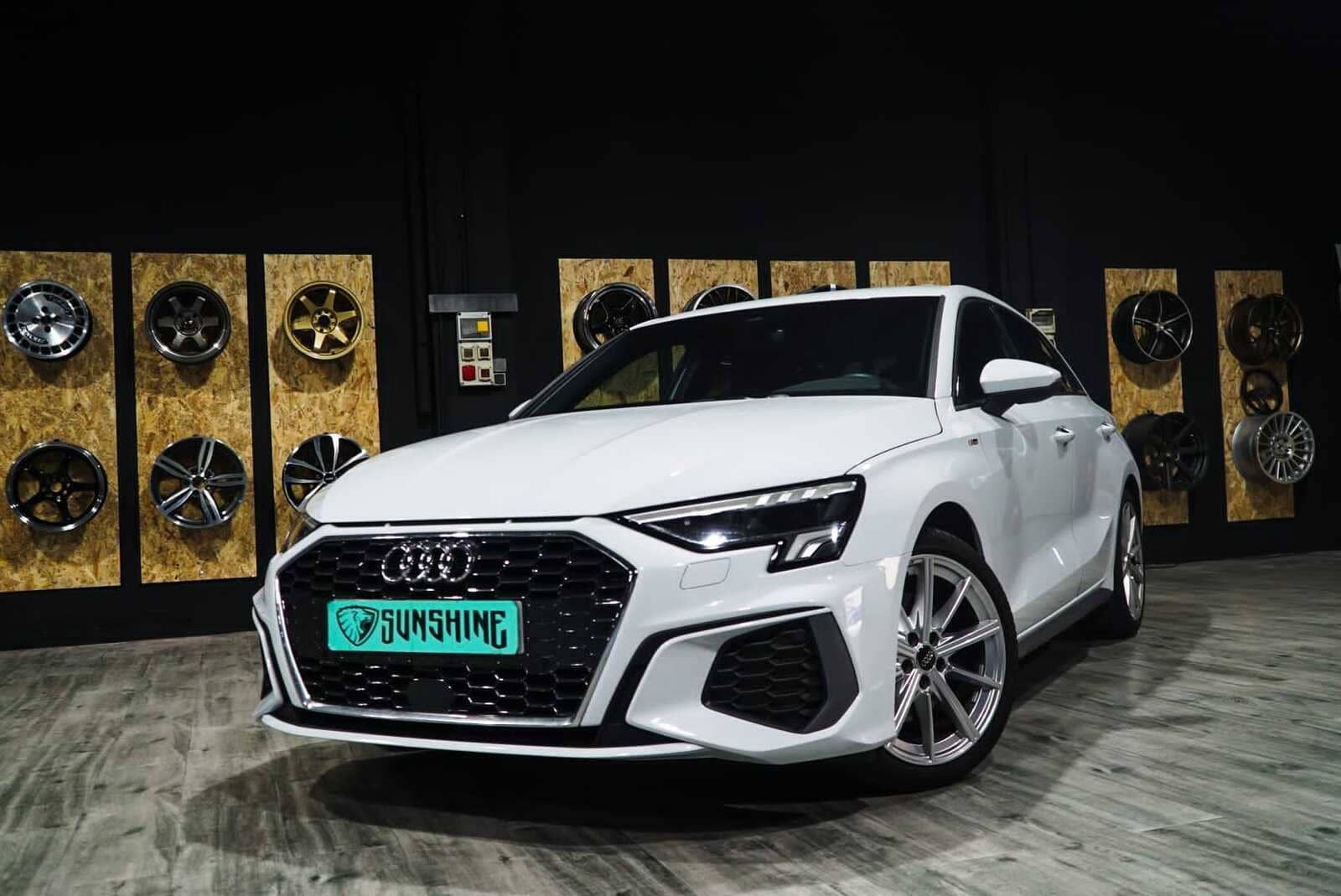 Un Audi A3 blanco está estacionado delante de un muro de ruedas.