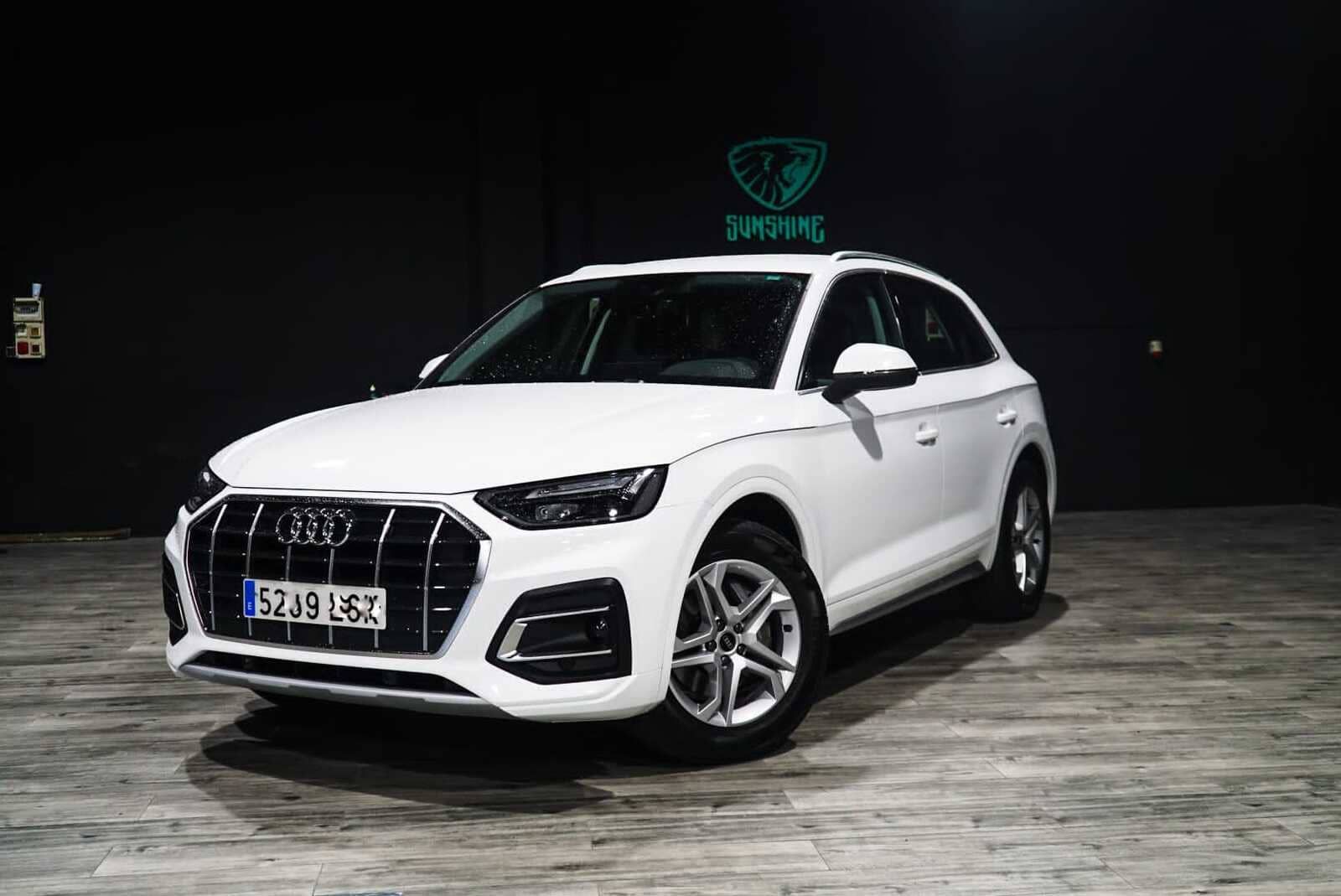 Un Audi Q5 blanco está estacionado sobre un piso de madera en una sala de exposición.