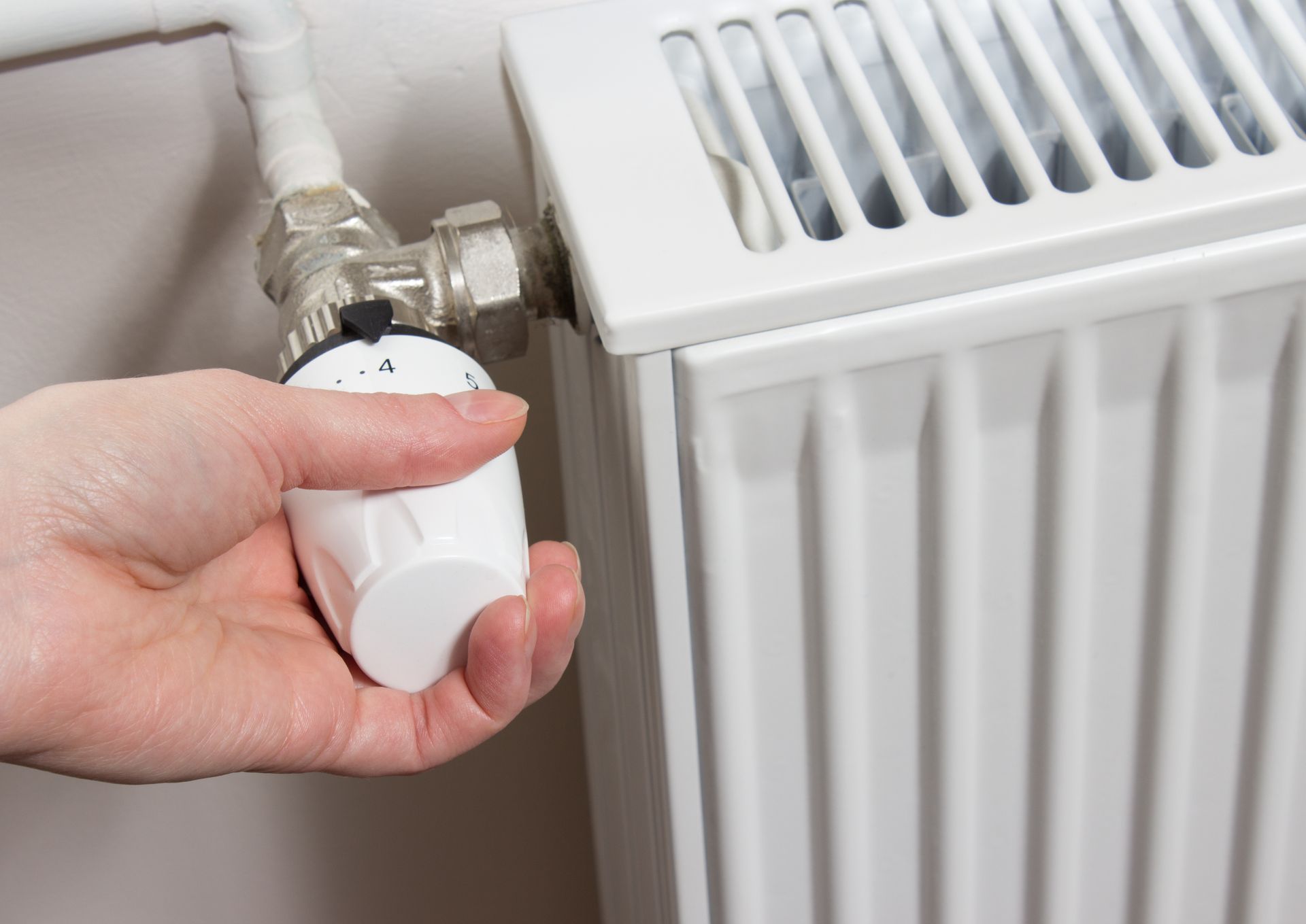 Manipulation manuelle d'un robinet de radiateur blanc à côté d'un panneau de chauffage blanc.