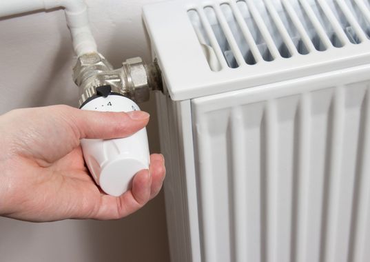 Manipulation manuelle d'un robinet de radiateur blanc à côté d'un panneau de chauffage blanc.