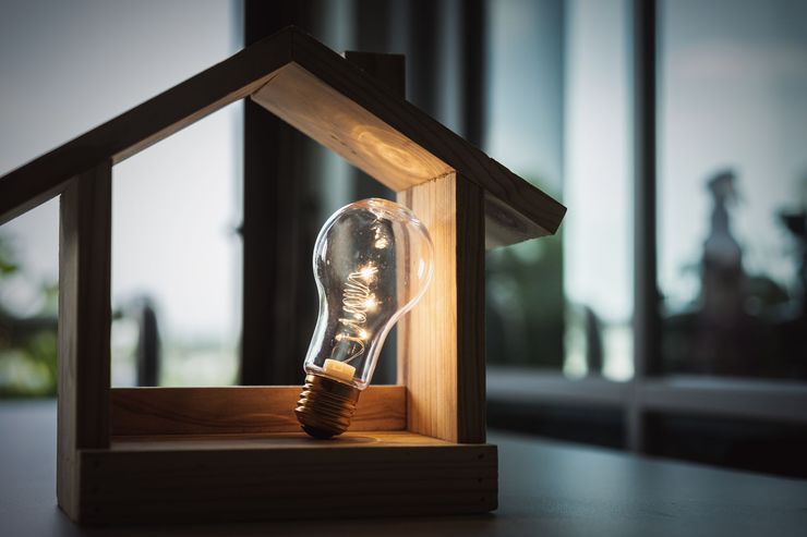 Une ampoule brille à l'intérieur d'une petite maquette de maison en bois près d'une fenêtre.
