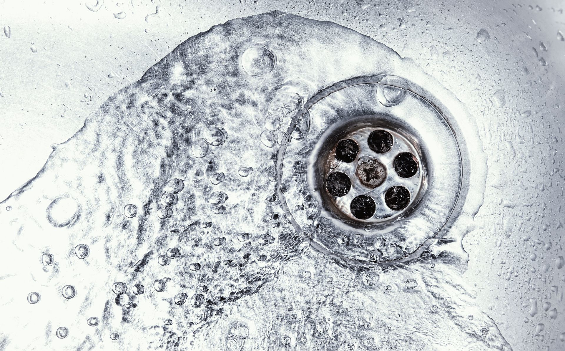 Gros plan sur une bonde d'évier métallique dépolie avec des gouttelettes d'eau à sa surface.