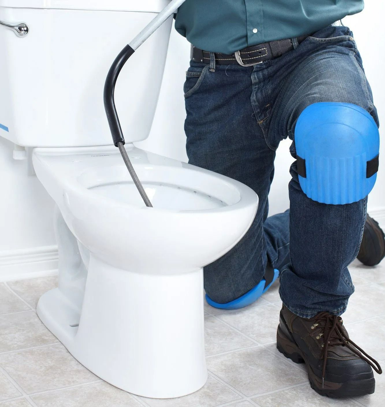 Un plombier agenouillé près des toilettes, utilisant une genouillère bleue pour réparer la plomberie de toilettes.