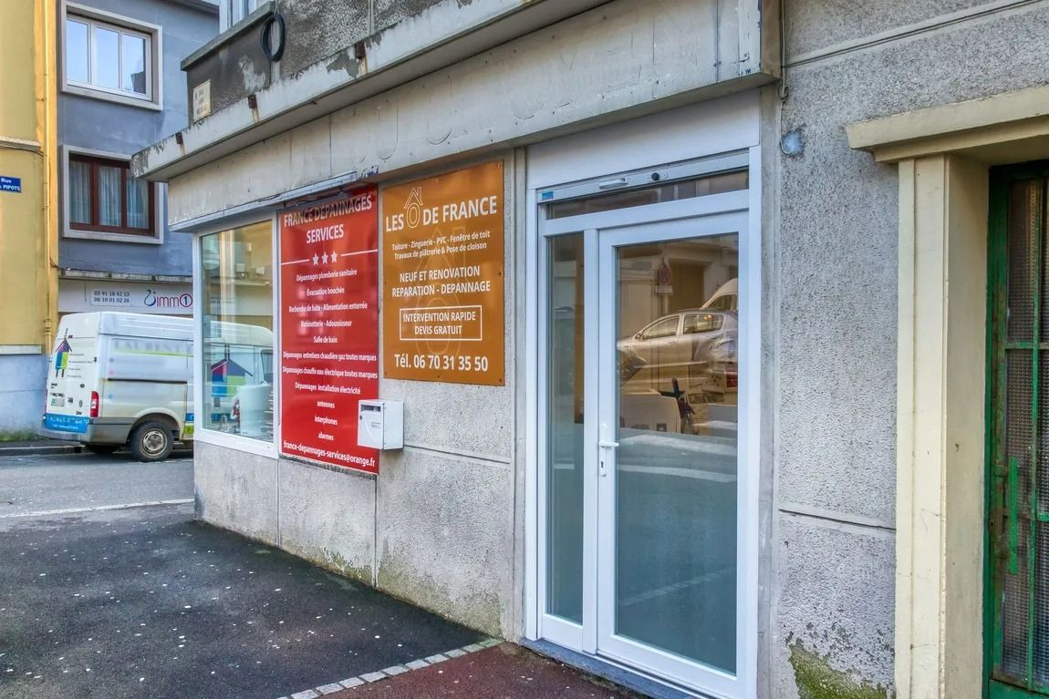 Boutique avec enseignes rouges et marron, porte blanche et façade en pierre, située dans une rue calme.