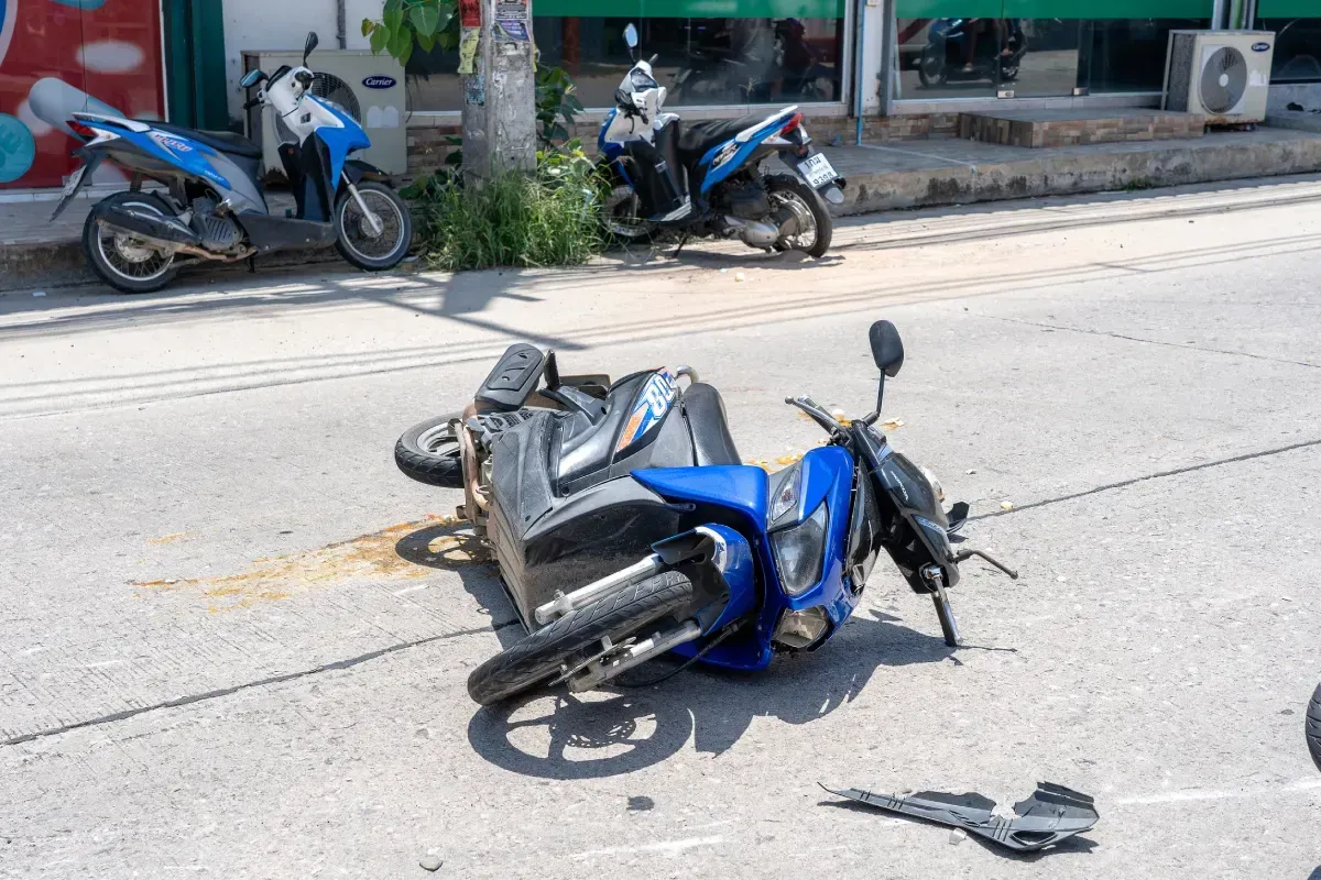 Una motocicleta azul volcó en una carretera asfaltada, posiblemente tras un accidente. Había otras motos estacionadas cerca.