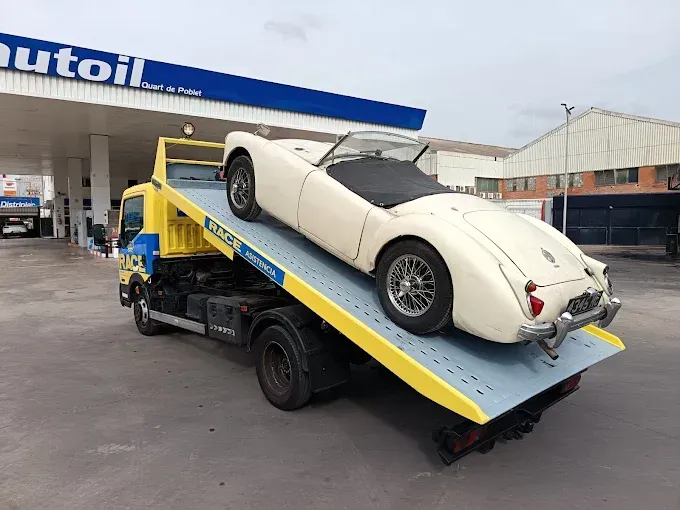 Un automóvil blanco está siendo cargado en una grúa al costado de una carretera.