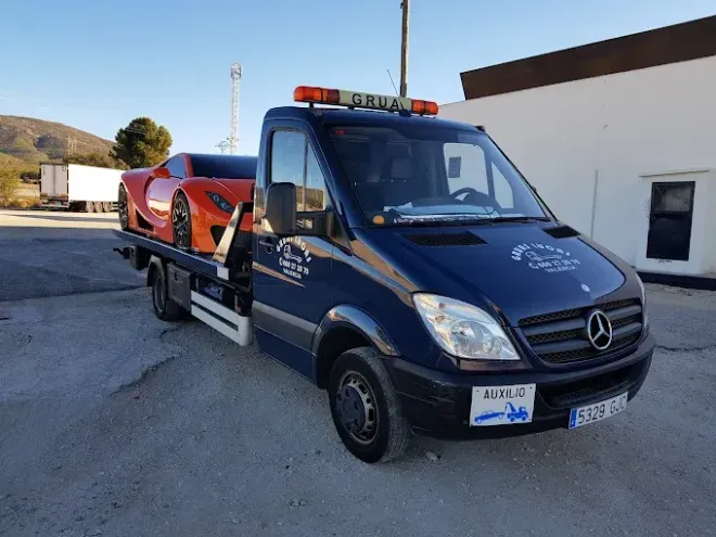 Un automóvil blanco está siendo cargado en una grúa al costado de una carretera.