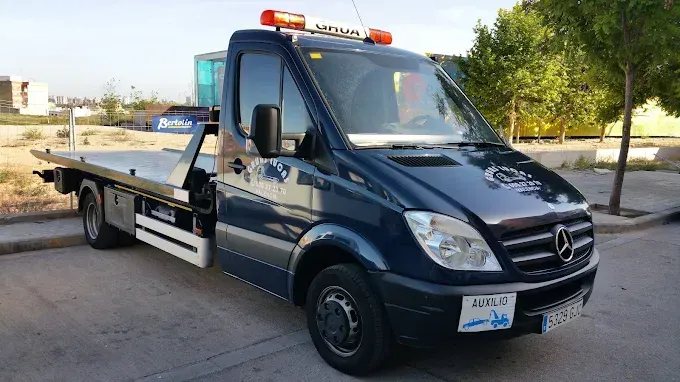 Grúa con grúa hidráulica, color azul y blanco, estacionada en una calle, sobre su plataforma se ve una motocicleta.