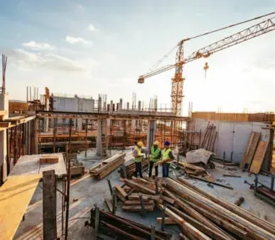 A group of construction workers are standing around a pile of wood at a construction site.