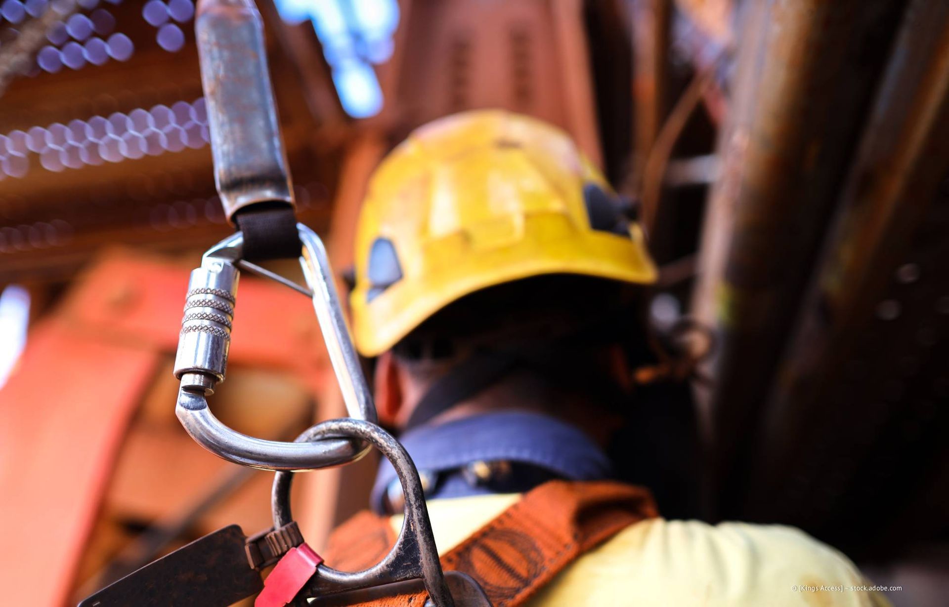 Gelber Schutzhelm, Gurtzeug und Karabiner; Arbeiter auf einer Baustelle.