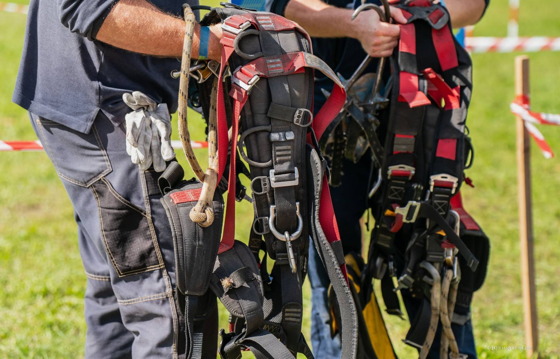 Zwei Personen halten im Freien Sicherheitsgurte, rot und schwarz, mit angebrachter Ausrüstung.