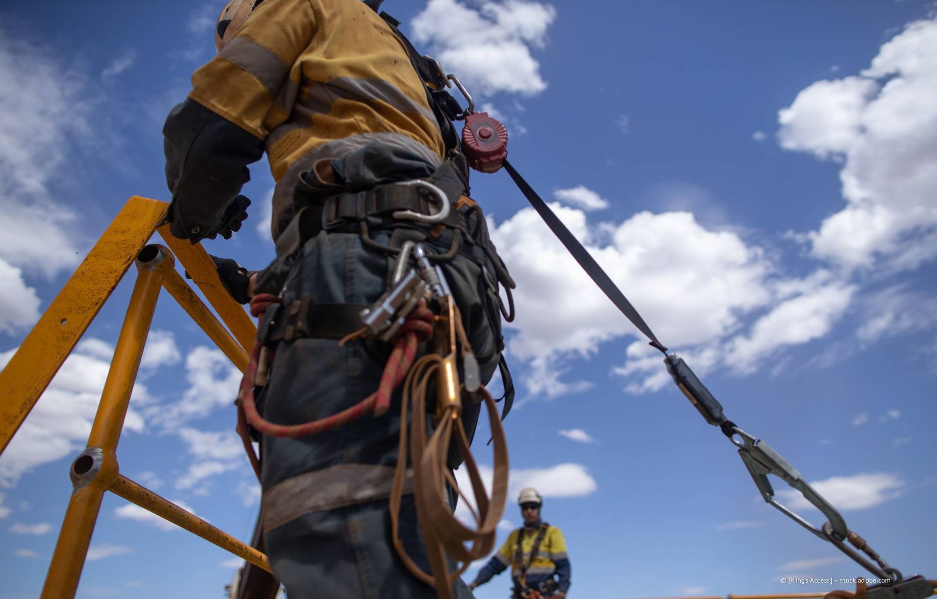 Arbeiter auf einem Dach, der einen Sicherheitsgurt an einer Rettungsleine trägt; blauer Himmel.