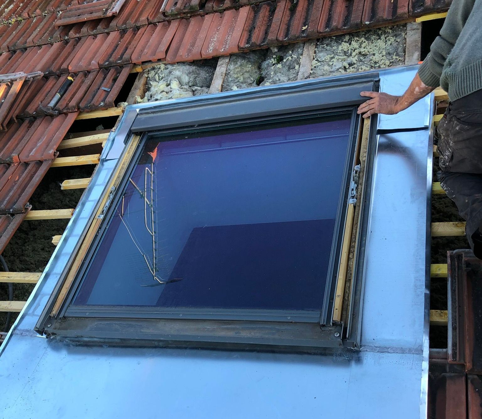 Un ouvrier pose une fenêtre sur un toit ancien