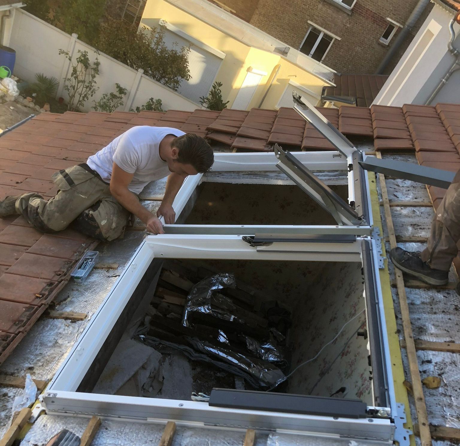 Un artisan pose une fenêtre de toit sur des tuiles en terre cuite