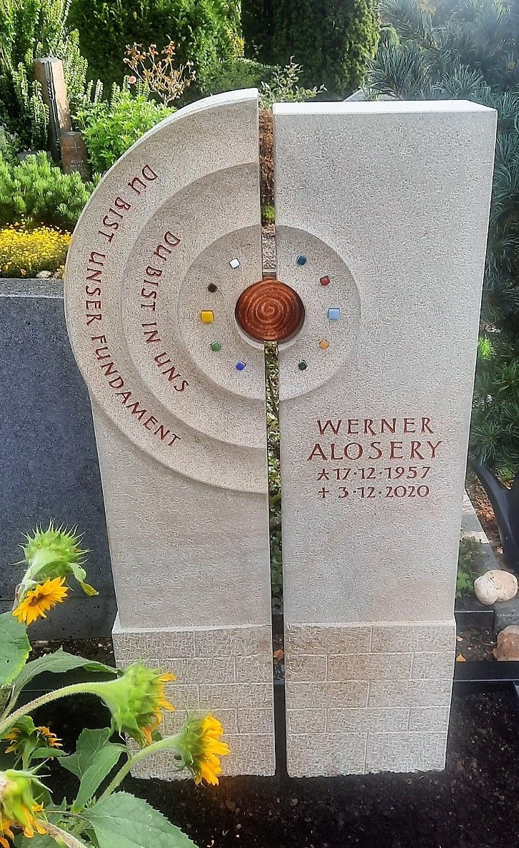 Ein Grabstein auf einem Friedhof mit Sonnenblumen im Hintergrund.