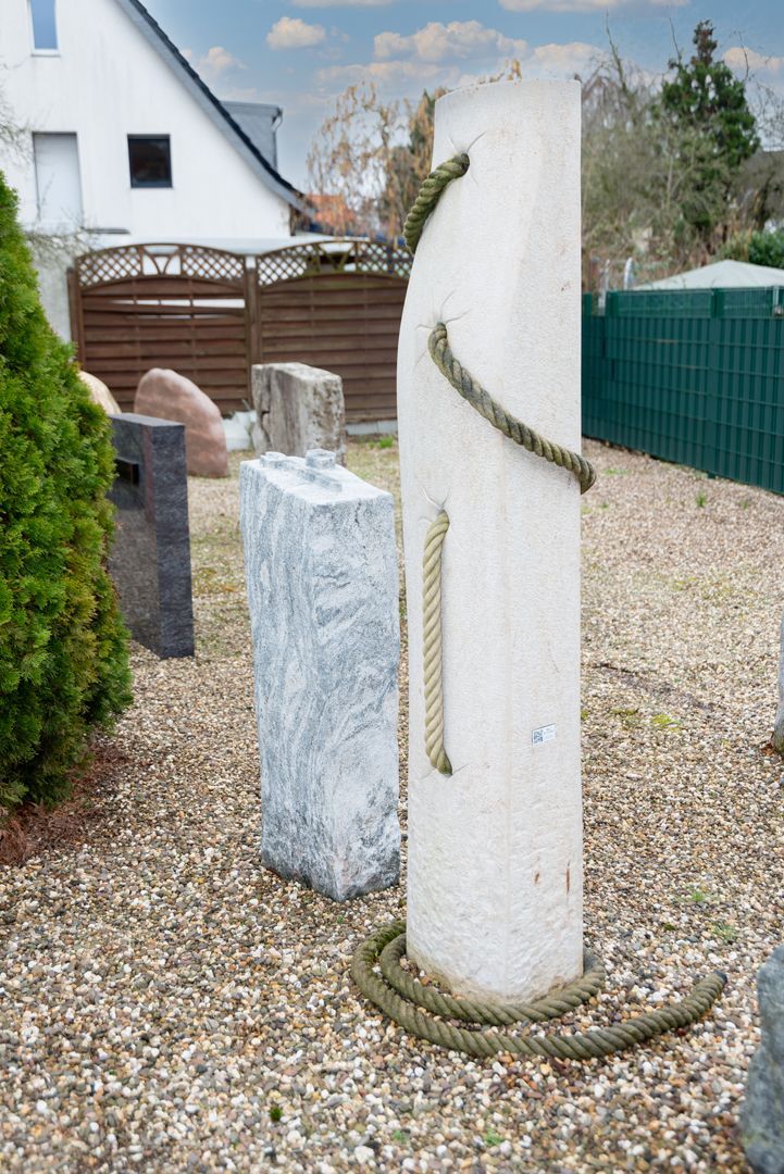 Eine weiße Skulptur mit einem Seil darum in einem Kiesplatz