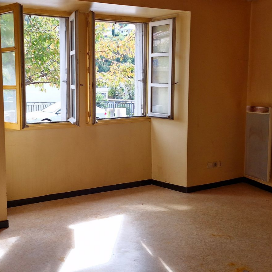 Pièce beige vide avec des fenêtres ouvertes et la lumière du soleil sur le sol.