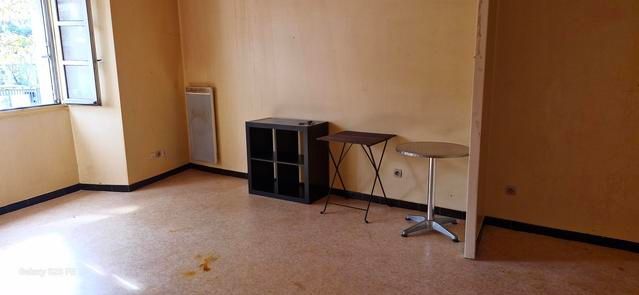 Pièce vide aux murs beiges, avec une fenêtre, une petite table et une étagère le long du mur.