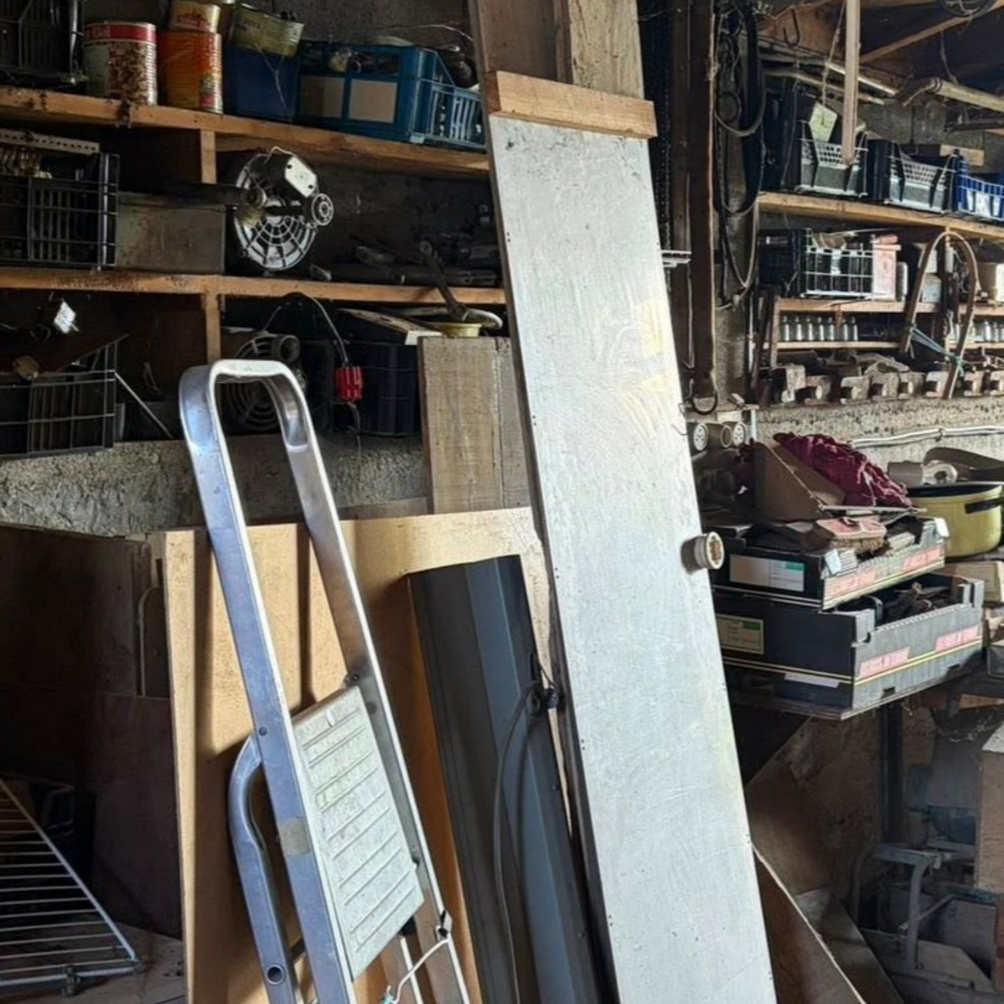 Atelier de garage avec des étagères, des outils et une grande planche appuyée contre une étagère.