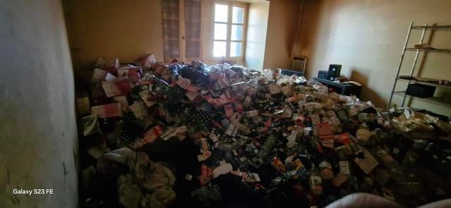 Pièce encombrée de tas d'ordures et de débris, avec des fenêtres à l'arrière laissant entrer la lumière du jour