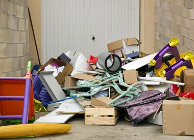 Des débris ménagers et des cartons s'entassent devant la porte du garage, mêlés à des meubles cassés et des tuyaux d'arrosage.