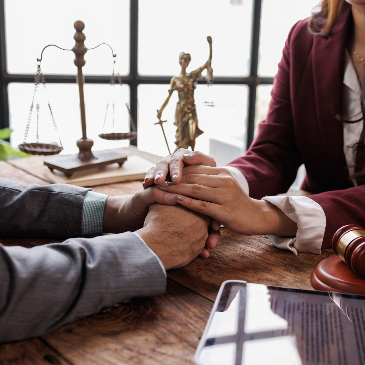 Un avocat réconforte son client, main dans la main, devant un bureau où se trouvent une balance de la justice et un maillet.