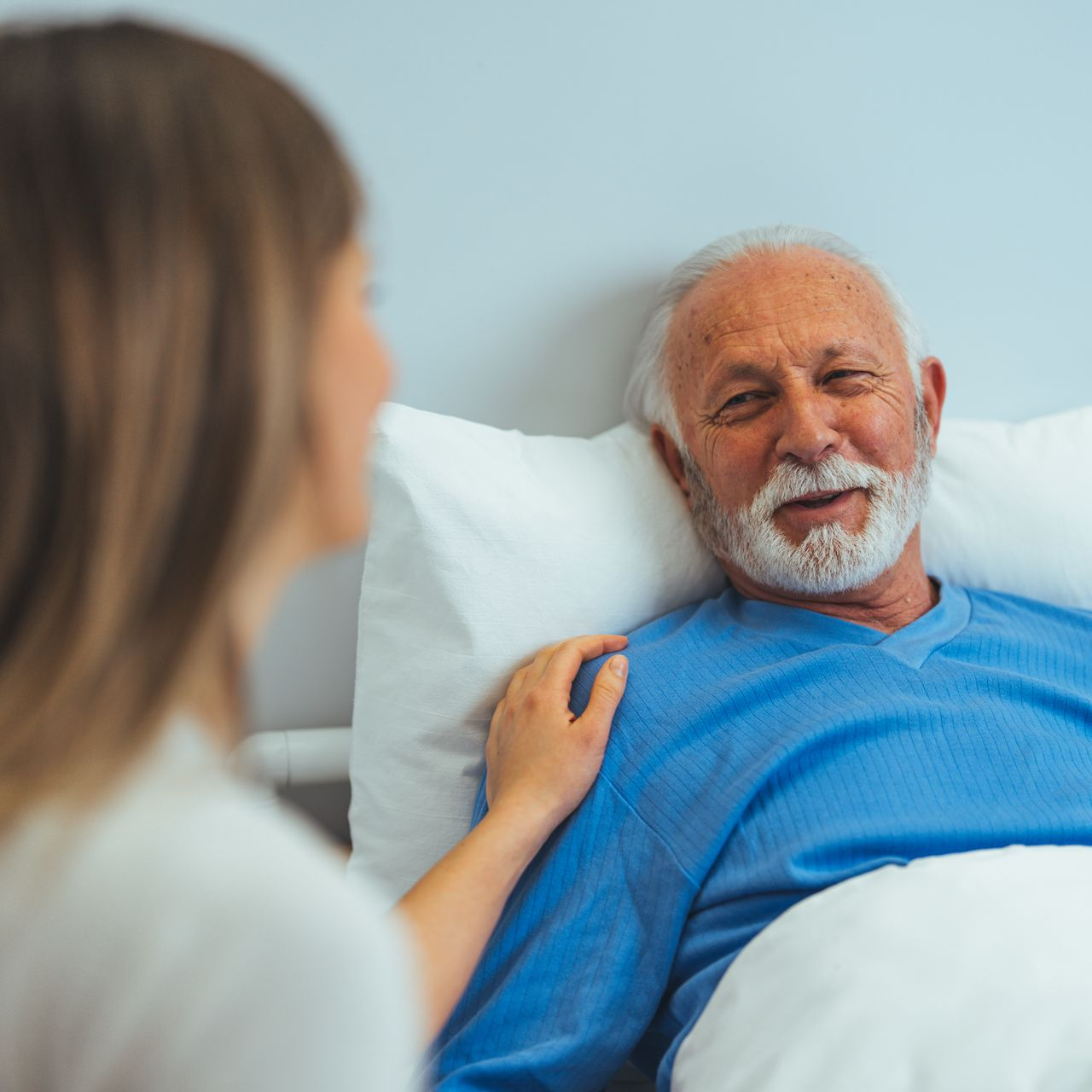 Une personne en tenue d'hôpital bleue sourit à quelqu'un qui a la main sur l'épaule.