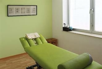 In einem Raum neben einem Fenster steht eine grüne Massageliege.