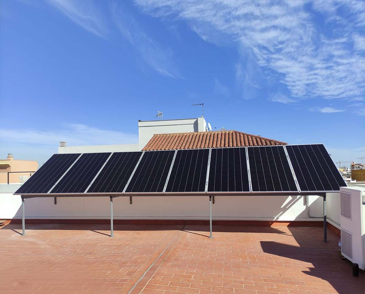 Paneles solares sobre un tejado de tejas de terracota contra un cielo azul con nubes tenues.