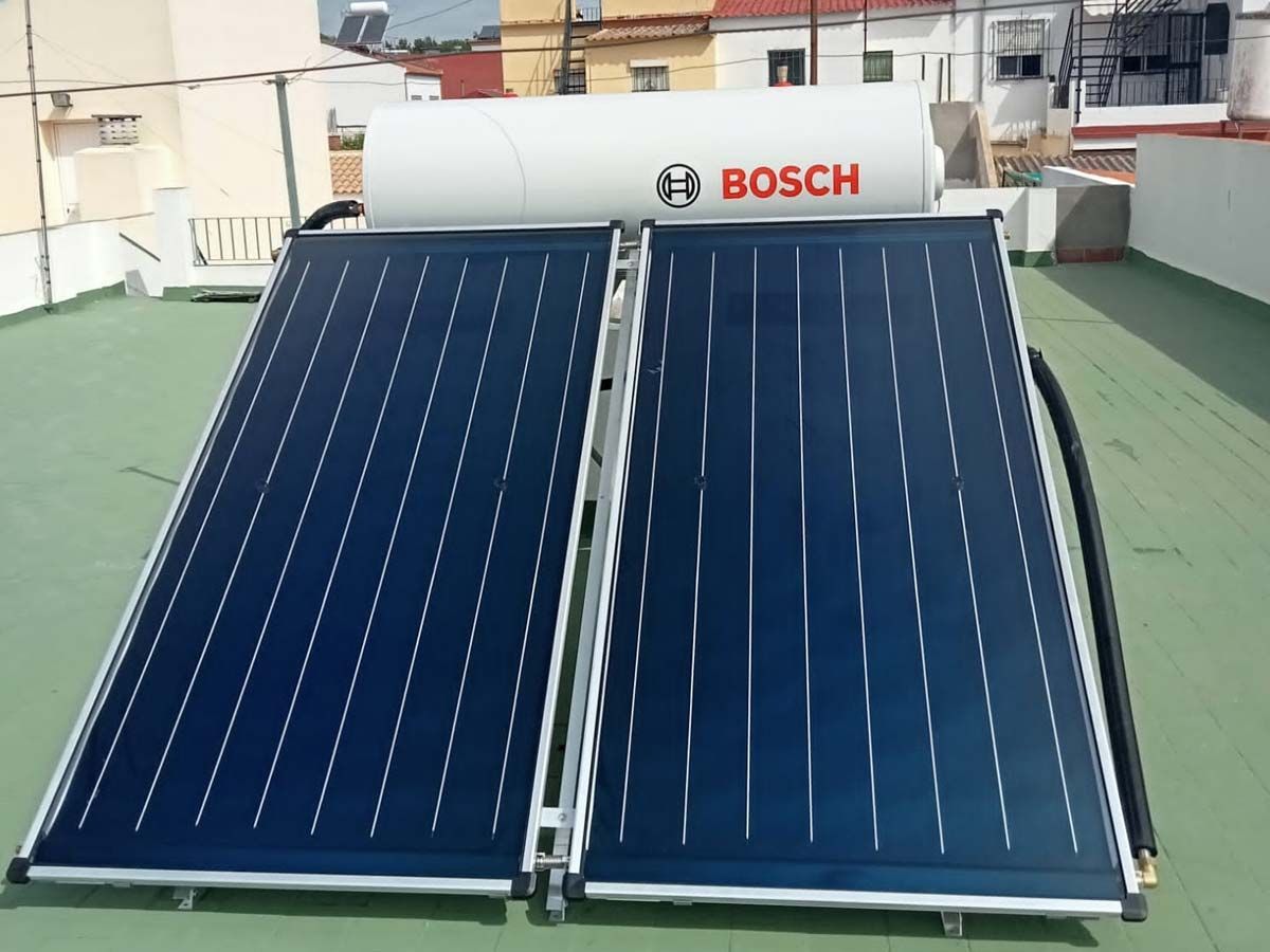 Sistema de calentador de agua solar en un tejado: tanque Bosch sobre dos paneles solares de color azul oscuro.