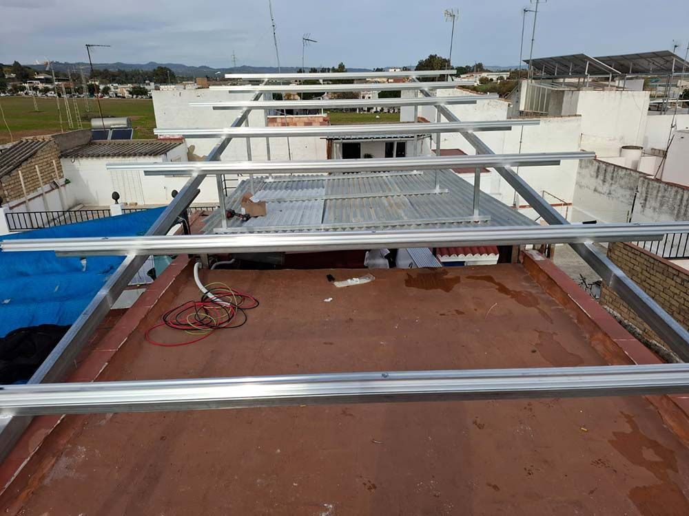 Marco de montaje para paneles solares que se construye sobre un tejado, con edificios circundantes visibles.