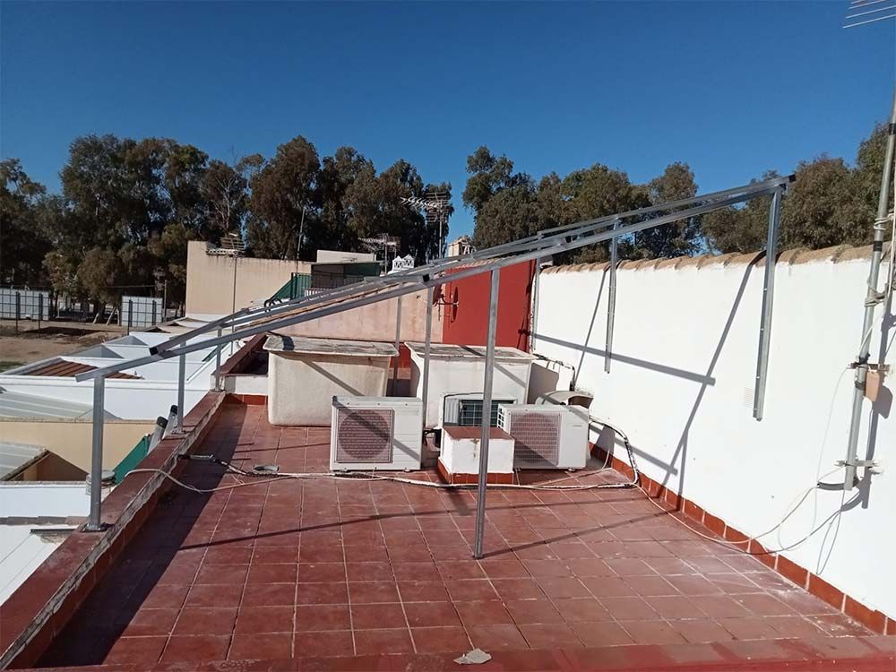 Estructura de marco de metal en la azotea con unidades de aire acondicionado contra una pared blanca, bajo un cielo despejado.