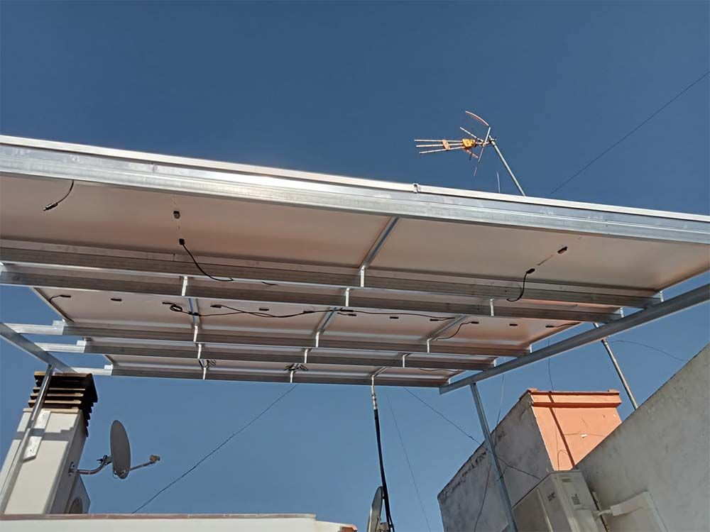 Paneles solares instalados en un marco de metal en un tejado, con una antena al fondo contra un cielo azul.