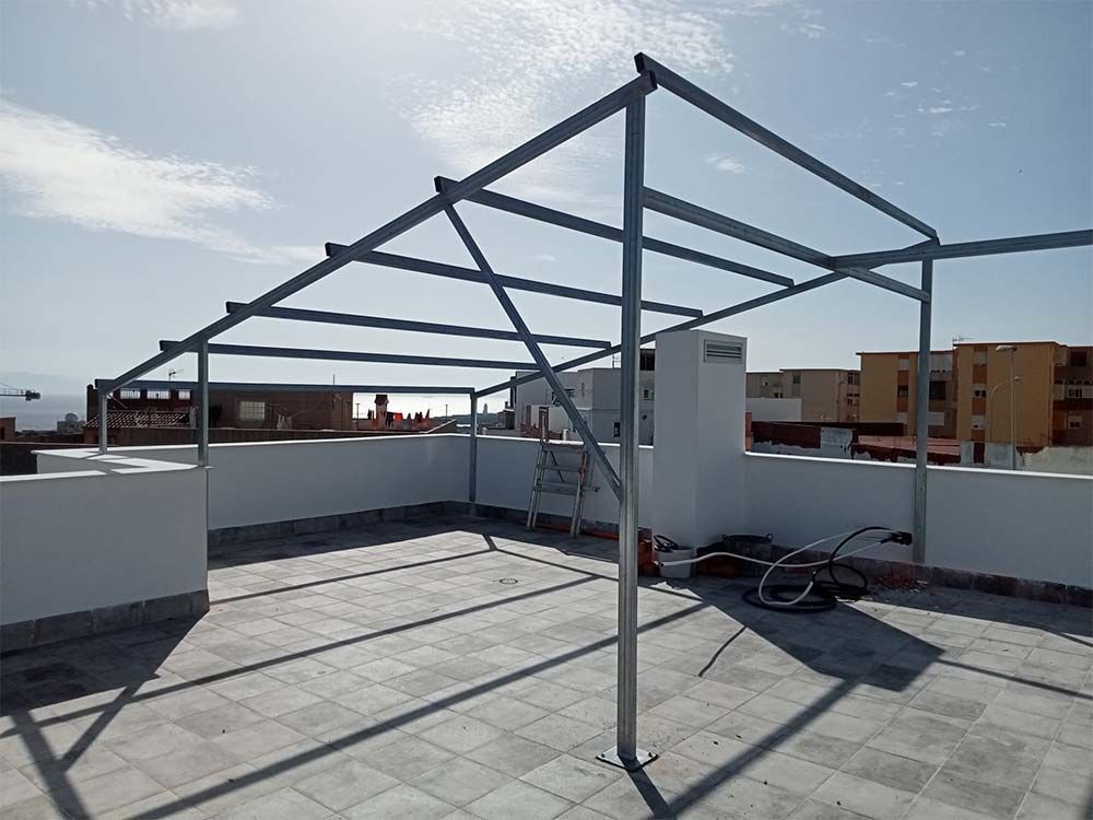 Estructura metálica de una pérgola en una azotea con un fondo de cielo azul soleado.