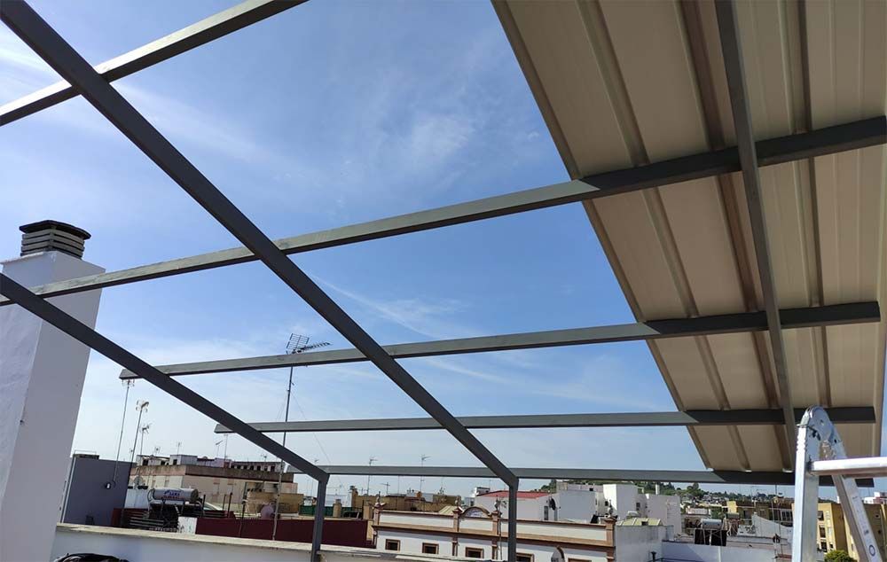 Techo con estructura de metal parcialmente cubierto con paneles blancos contra un cielo azul.