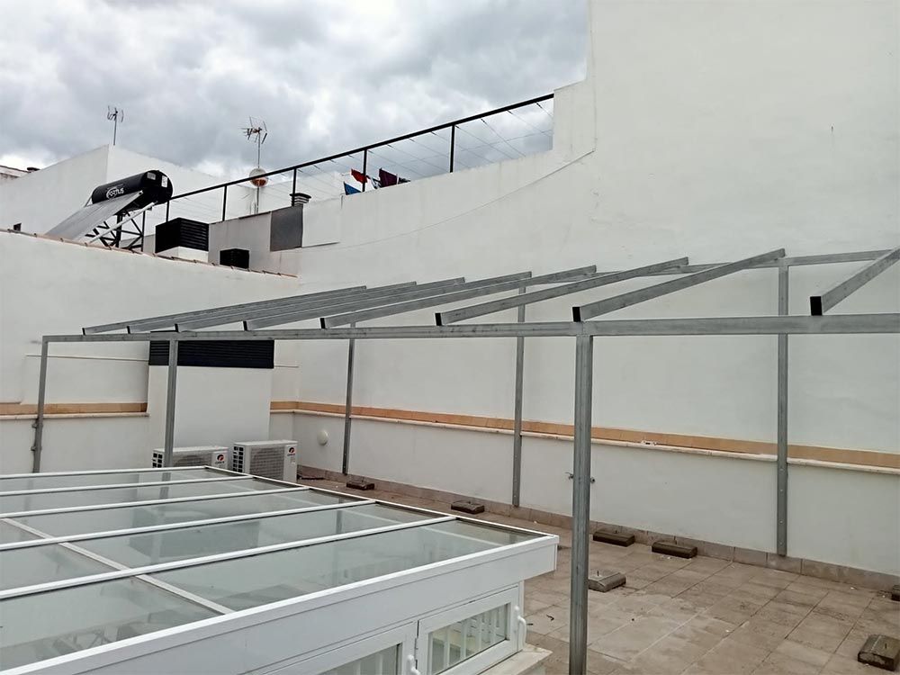 Estructura de marco de metal que se instala en una azotea, con un techo de paneles de vidrio debajo y paredes blancas.