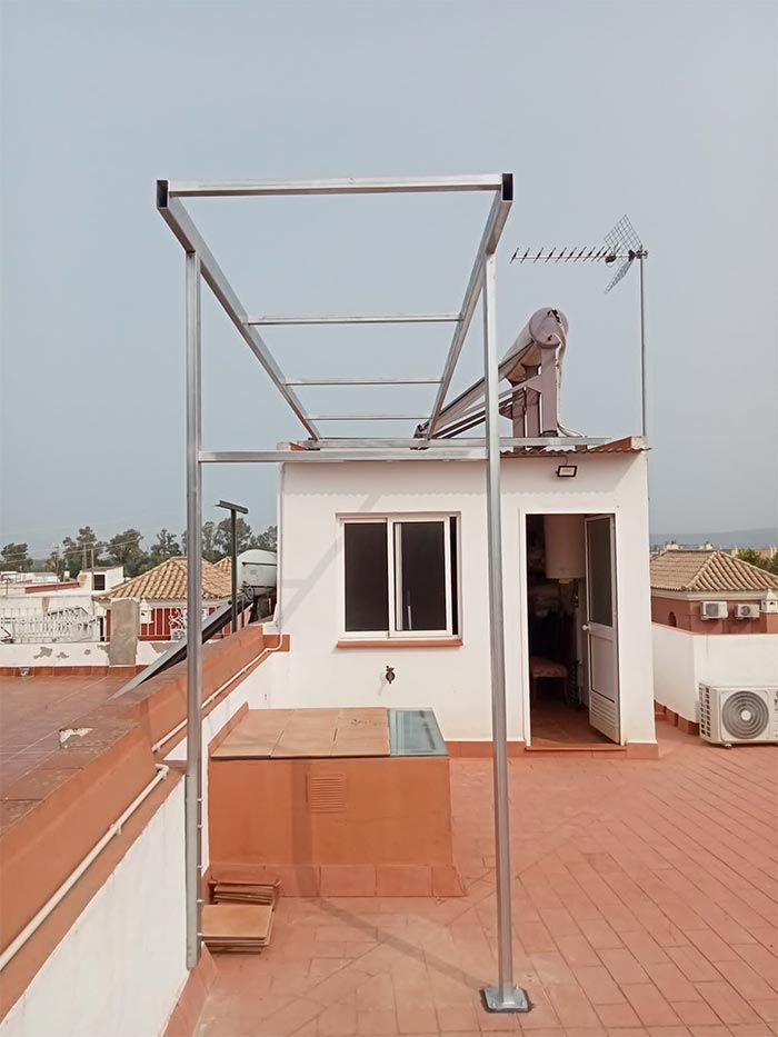 Tendedero metálico en una azotea con vistas a un pueblo. Luz solar brillante y cielo despejado.