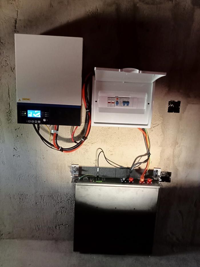 Inversor solar, panel eléctrico y batería montados en una pared de hormigón rugoso con cableado conectado.