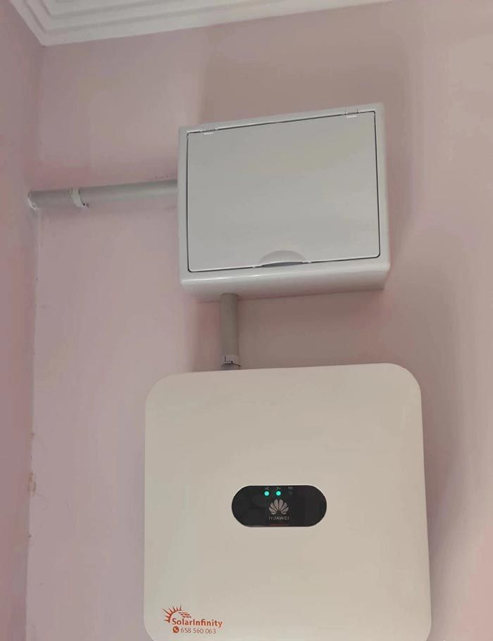 Inversor solar Huawei blanco y caja eléctrica montados en una pared rosa. Un conducto los conecta.