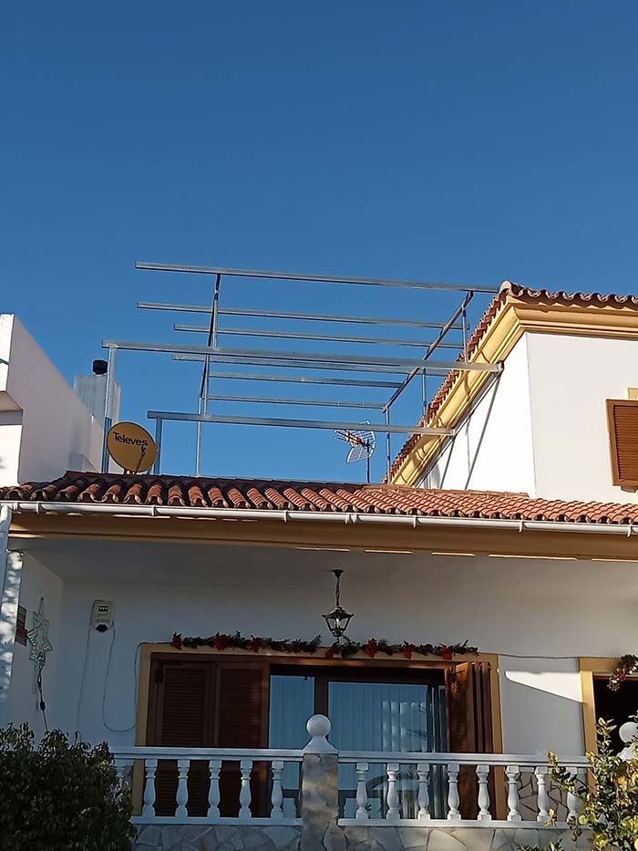 Estructura de marco de metal en la azotea de una casa blanca con techo de tejas de terracota y un fondo de cielo azul claro.